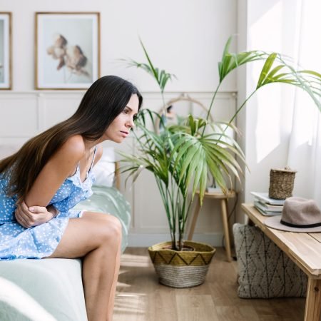 Young adult woman suffering from stomach ache on bed at home